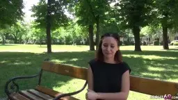Rothaarige junge Frau lächelt auf Parkbank, grüne Bäume im Hintergrund