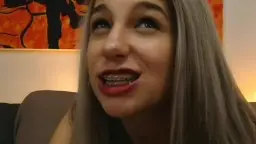 Silberhaarige Camgirl mit Headgear lächelt auf Sofa
